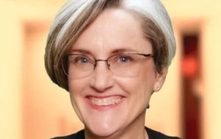 Smiling woman with short, gray hair and eye glasses.