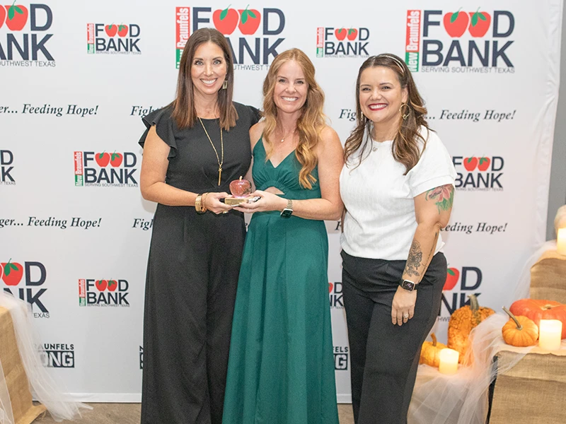 Three women pose in front of photo backdrop.