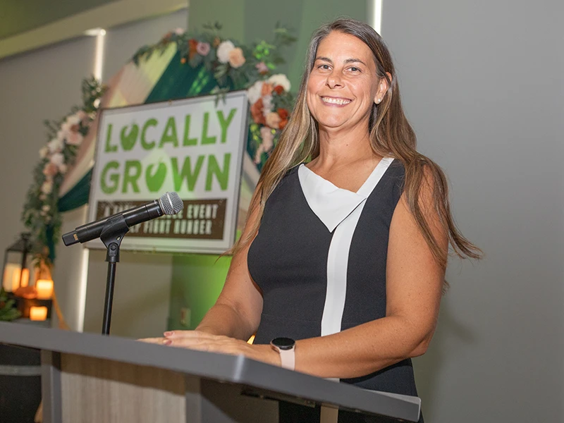 Woman stands at a lectern and smiles toward the camera.