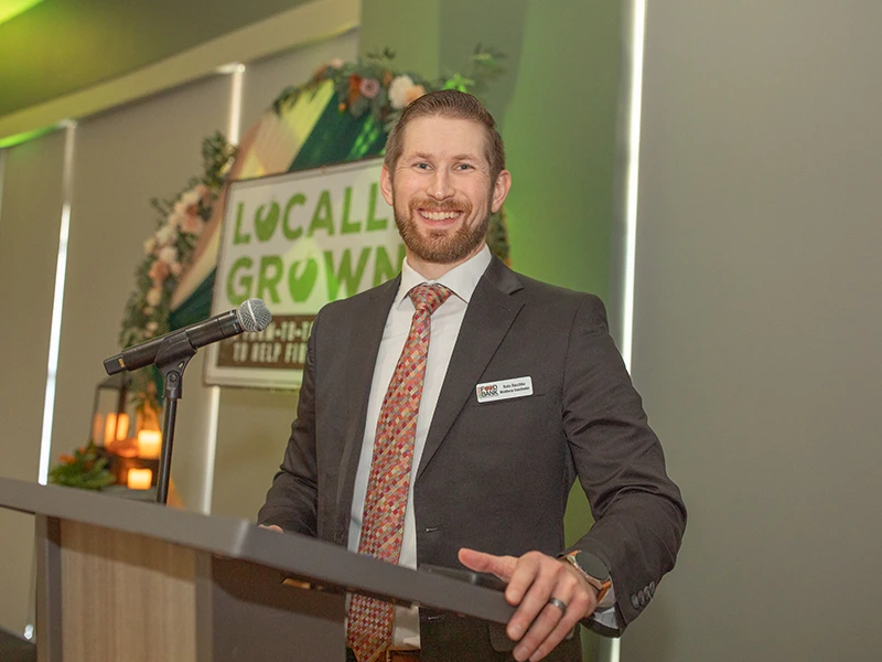 Smiling man in suit stands at a lectern.